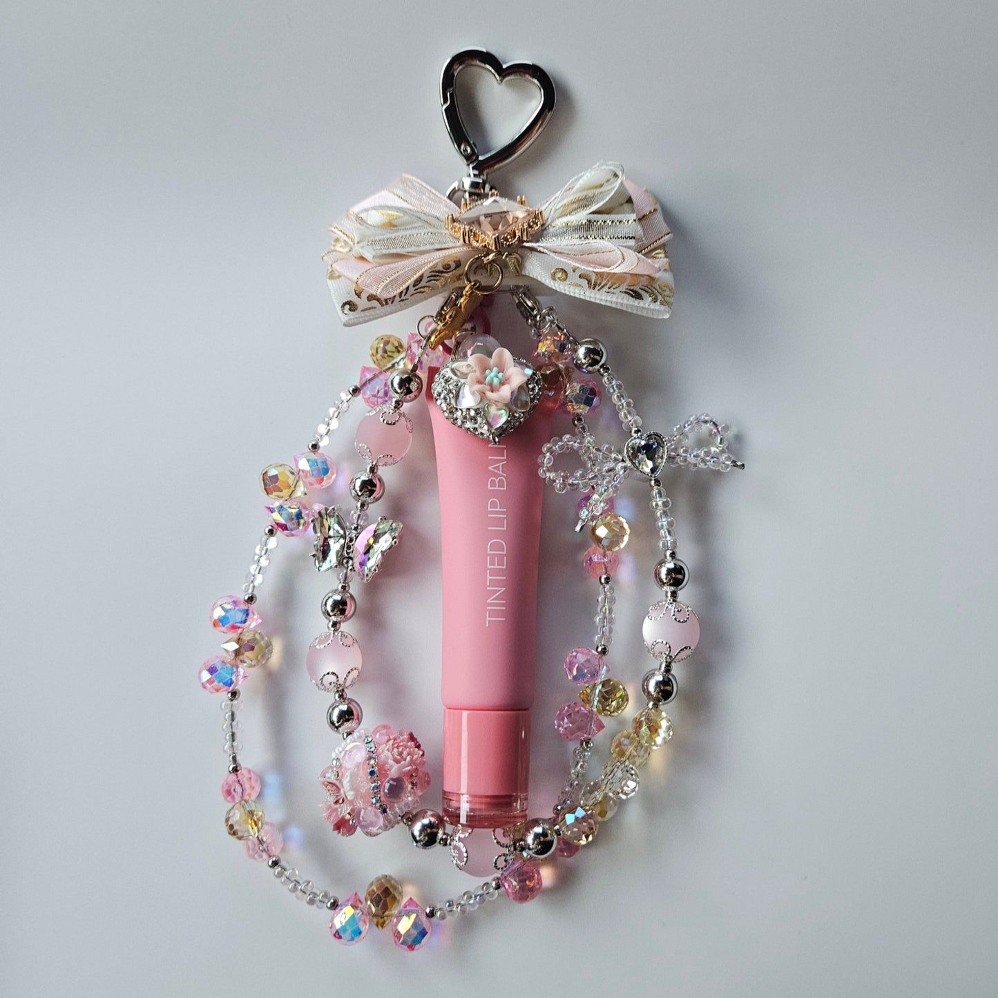 Pink lip balm with decorative chain on a light gray background