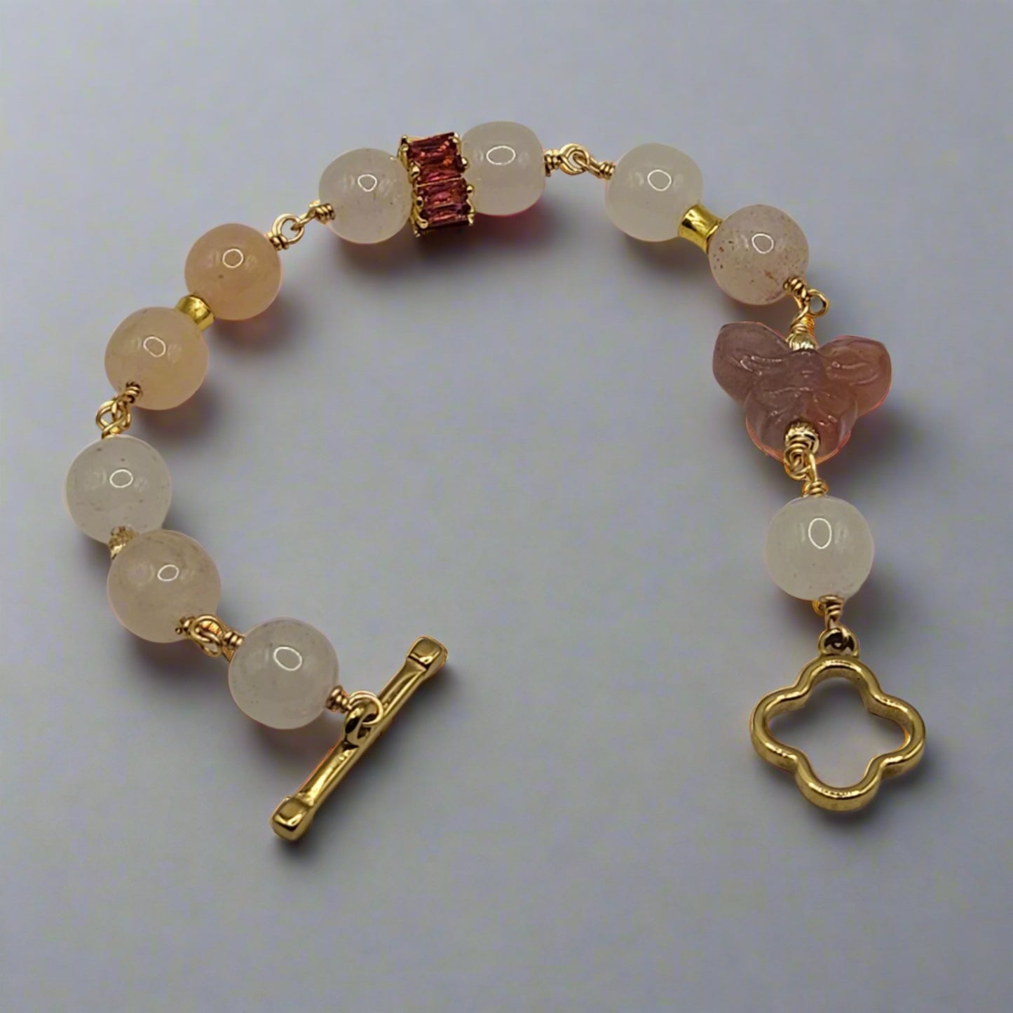 Bracelet with light-colored beads and gold accents on a light gray background