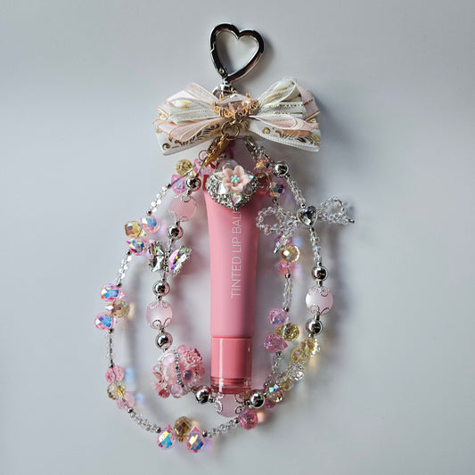 Pink lip balm with decorative chain on a light gray background
